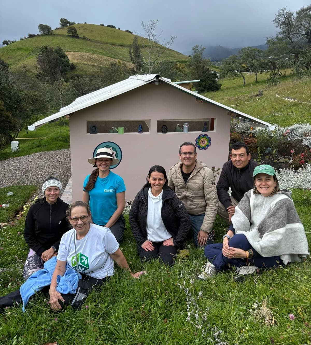 Grupo de personas frente a una construcción rodeada de colinas verdes.